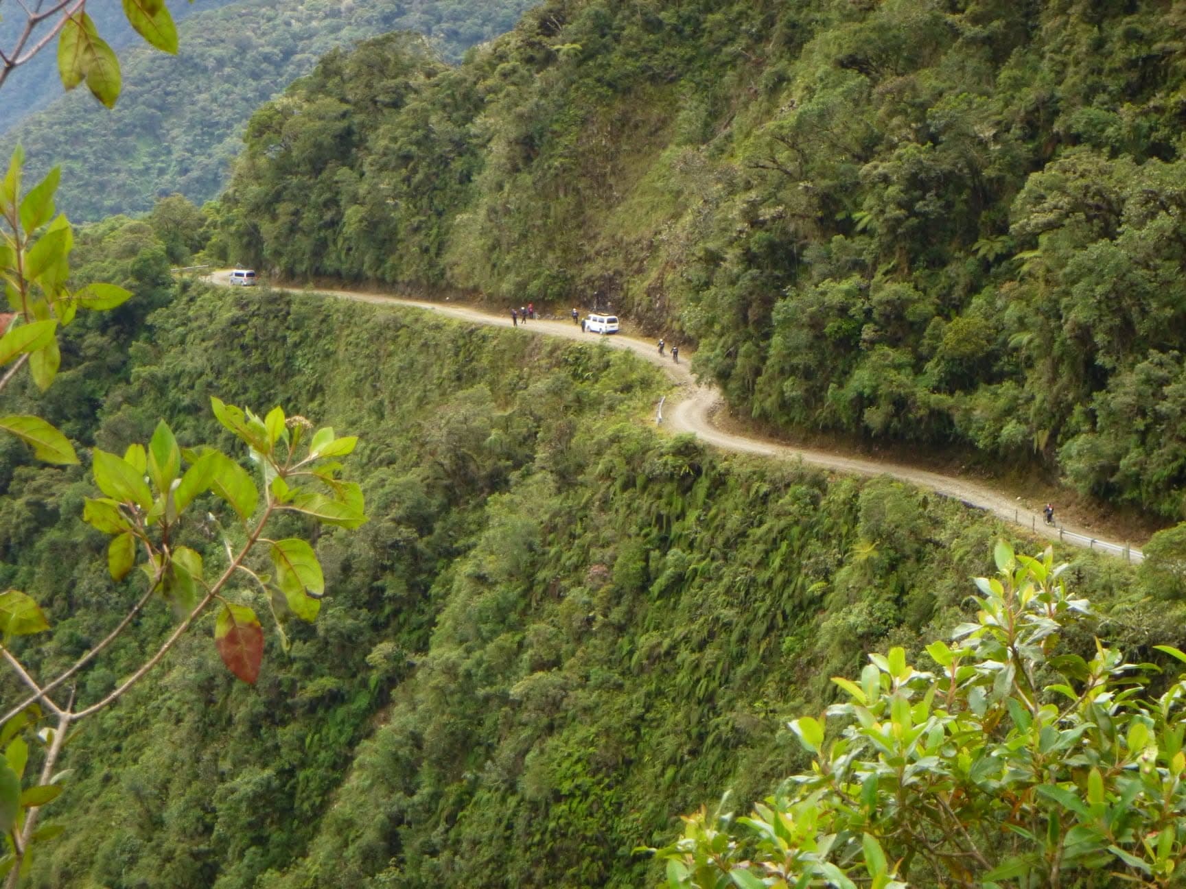 A van and cyclists on the winding North Yungas Road carved into a green Bolivian mountainside